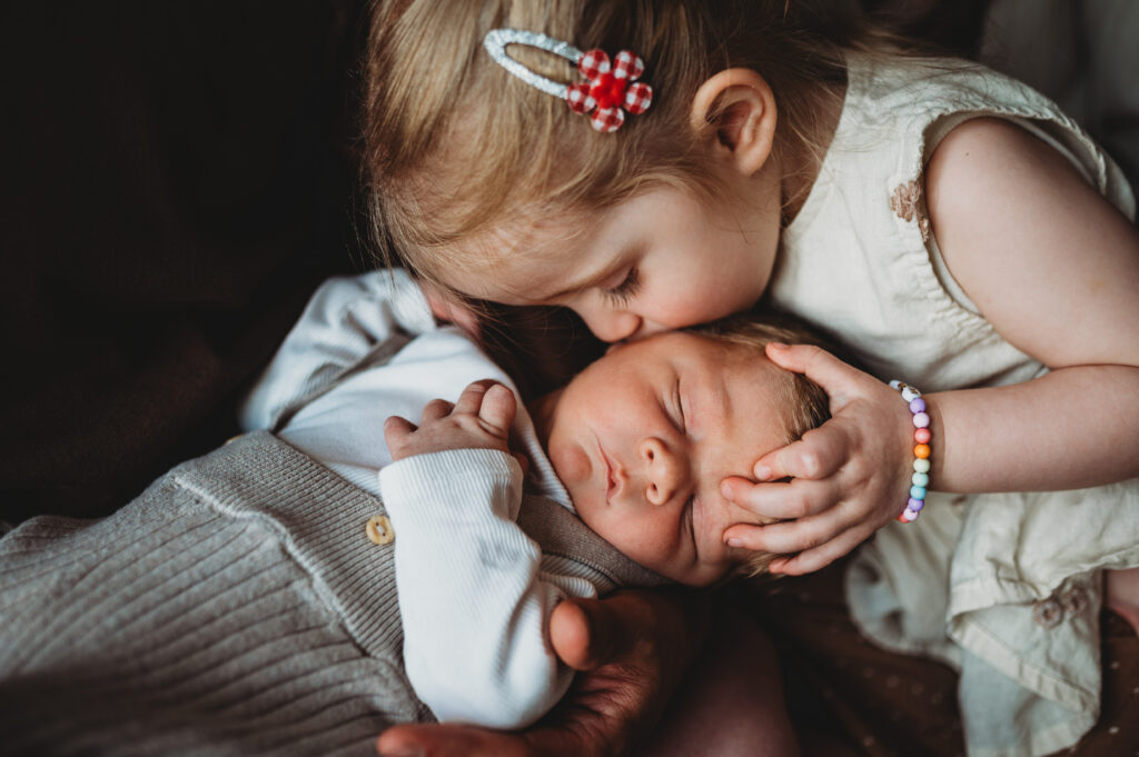 große Schwester küsst den neugeborenen kleinen Baby Bruder