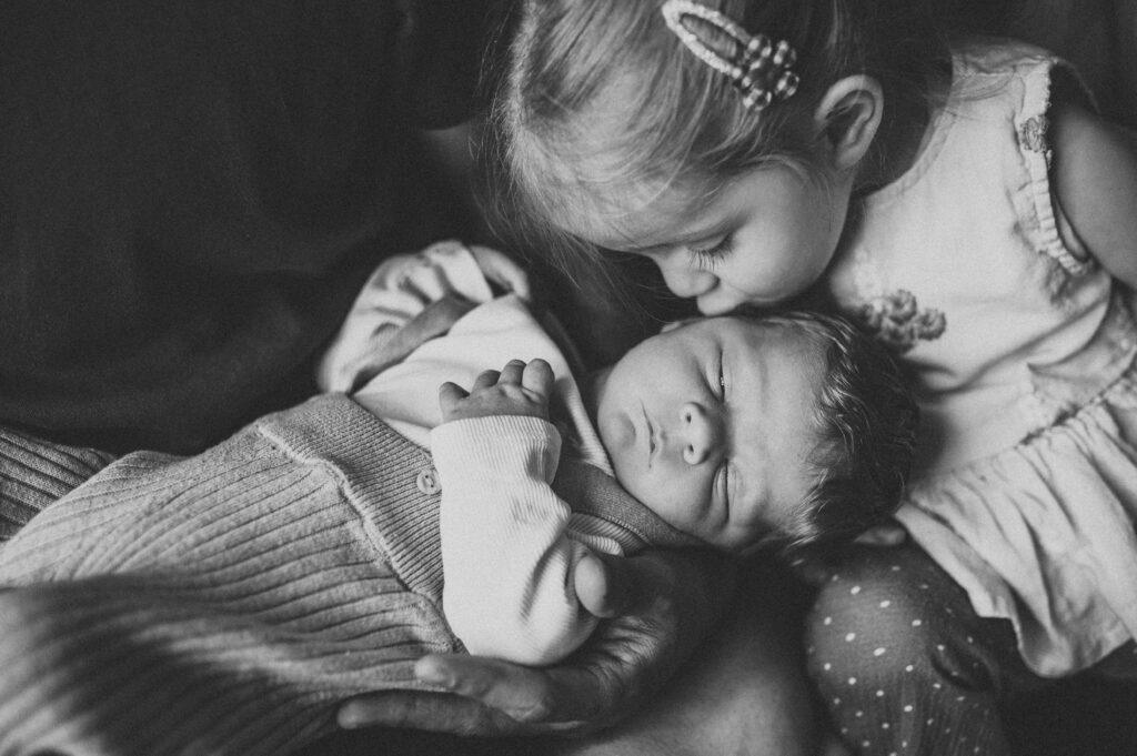 große Schwester küsst den neugeborenen kleinen Baby Bruder